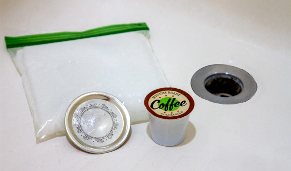 Coffee Pod, Plastic bag, and container lid next to a bath drain