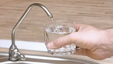 Hand holding a small glass under a faucet for filtered water as water streams into glass.