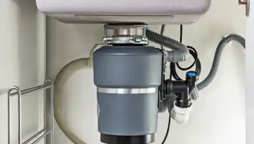 A garbage disposal unit mounted in the cabinet space below a residential sink.