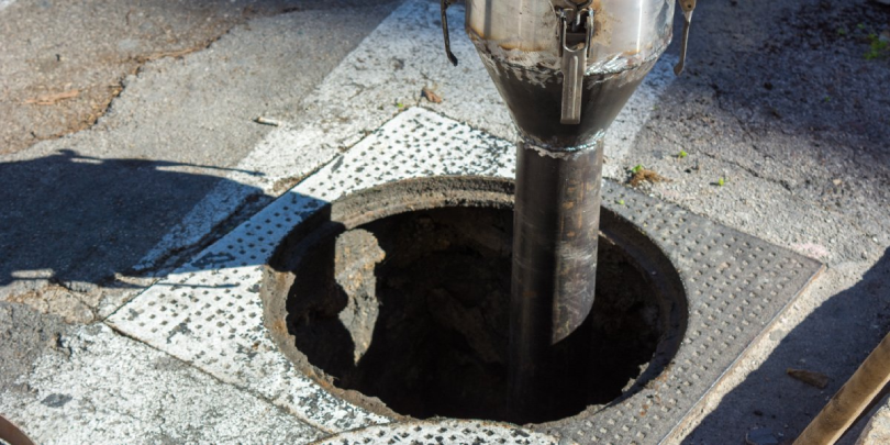 An open sewer cover and a machine inserted inside for the purpose of sewer cleaning in Calgary, AB