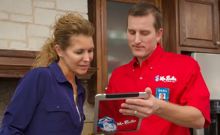 A plumber from Mr. Rooter Plumbing and a homeowner looking at a tablet as they discuss information about plumbing services.