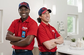 Two Mr. Rooter professionals standing in a bathroom with their arms crossed.