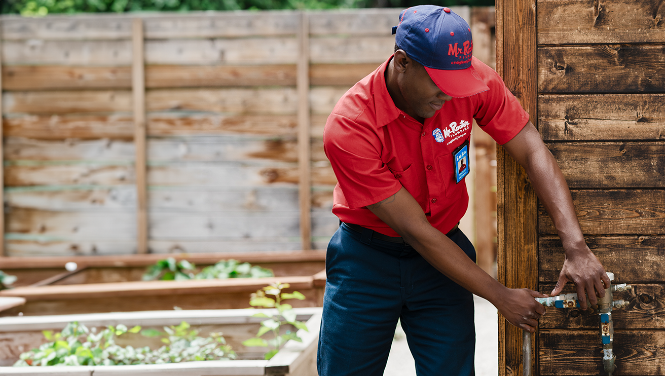 Mr. Rooter technician repairing a backflow preventer on the exterior of a home.