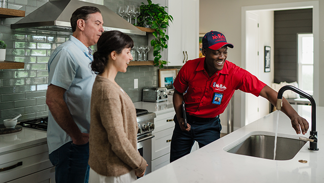 Mr. Rooter professional checking a sink faucet with two customers.