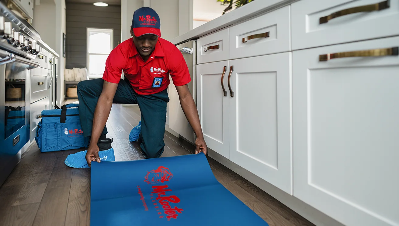 Mr. Rooter technician rolling out a rug in a kitchen to prepare for work.