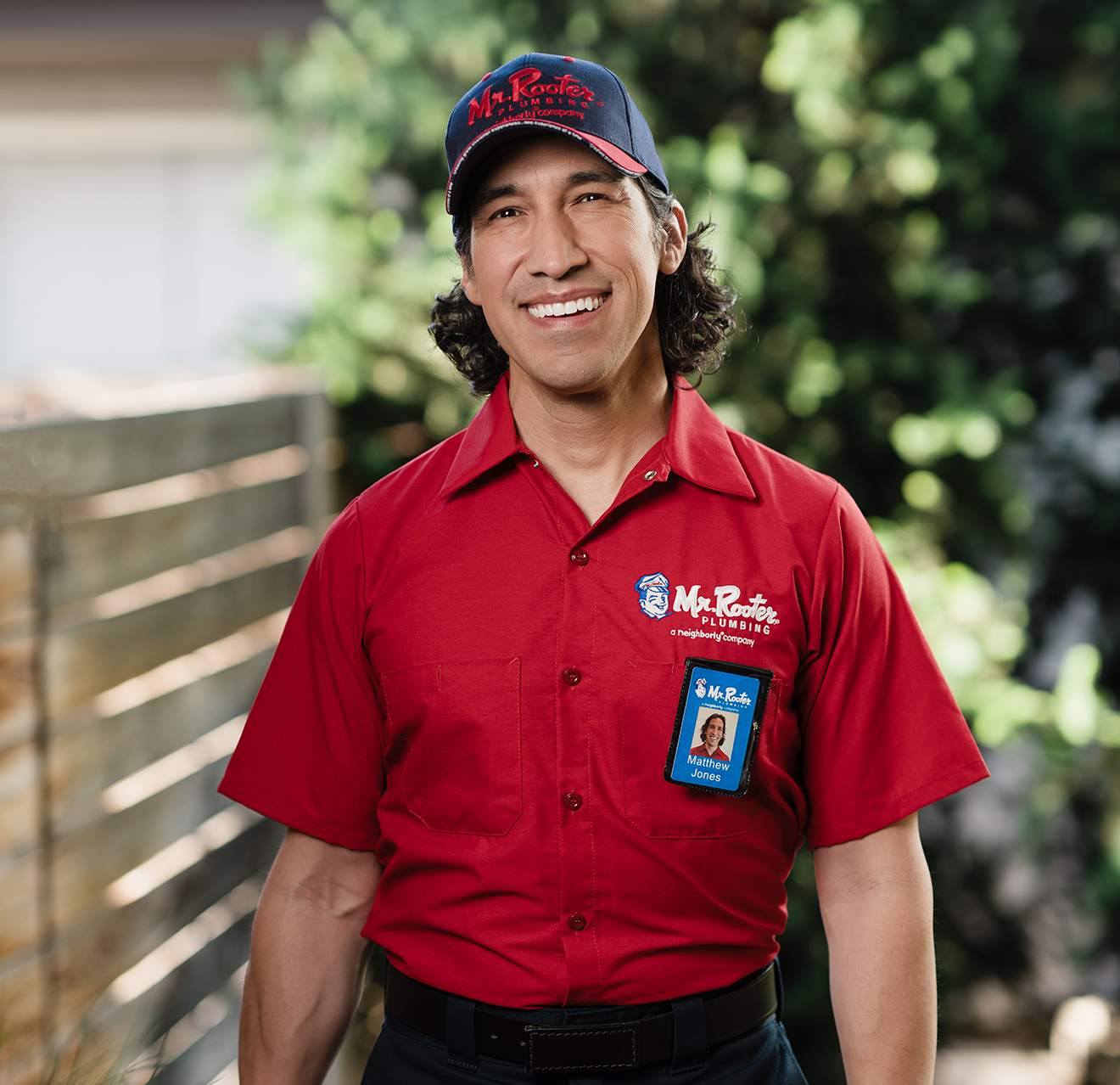 Portrait of a smiling Mr. Rooter technician with greenery in the background.