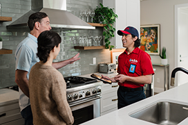 Mr. Rooter technician speaking with two customers in a modern kitchen.