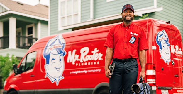 Mr. Rooter Plumbing technician standing beside a branded work van.