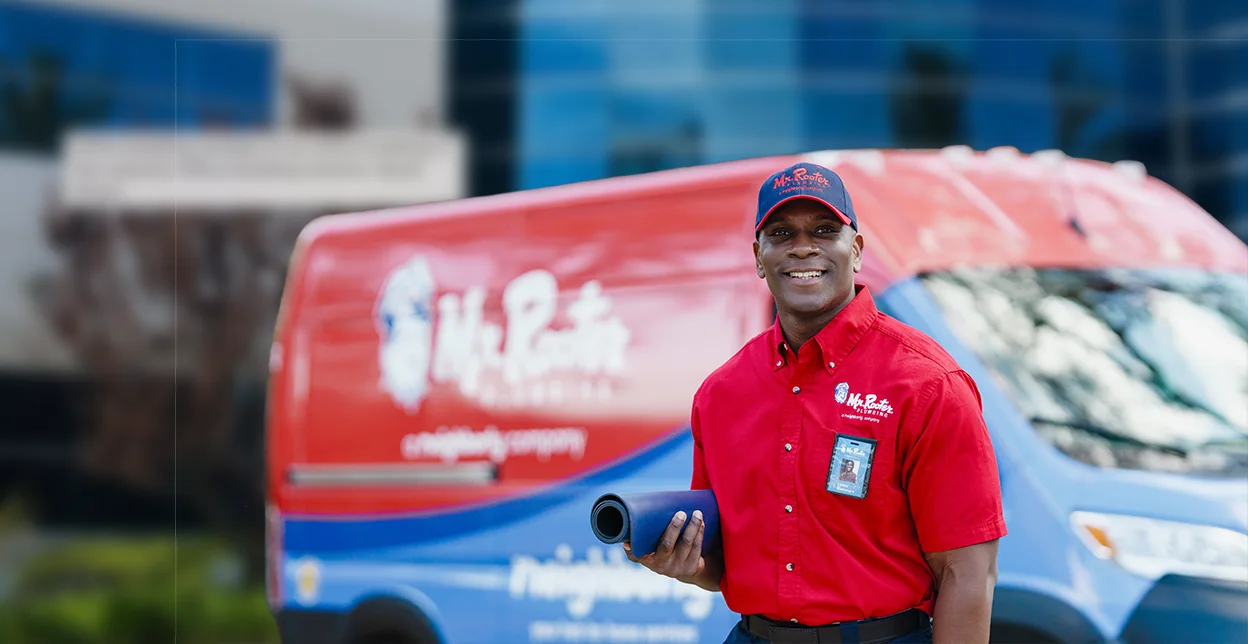 Mr. Rooter technician standing in front of a branded work van.