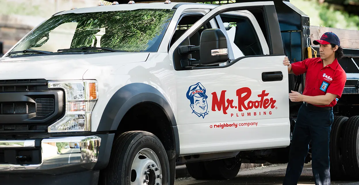 White Mr. Rooter truck parked with technician standing beside it.