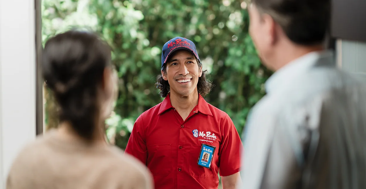 Two customers greeting a Mr. Rooter tehcnician at their front door.