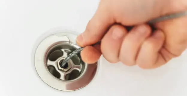 A plumber using a drain snake to clear out a drain at the bottom of a sink during an appointment for drain cleaning in Calgary.