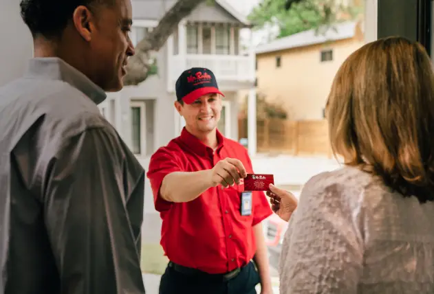 Mr. Rooter service professional holding out his card to a couple at their door.