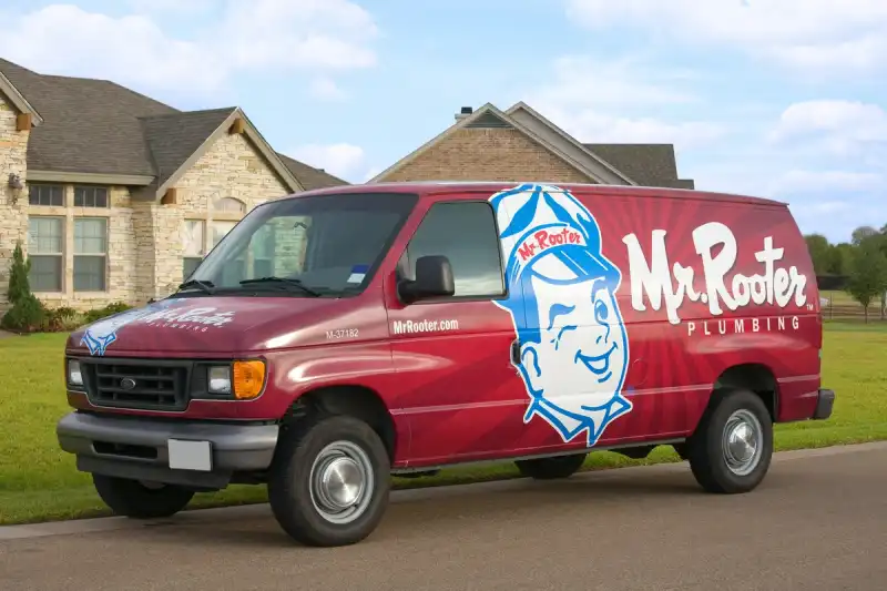 Mr. Rooter Plumbing van parked on street with two large brick homes behind it.