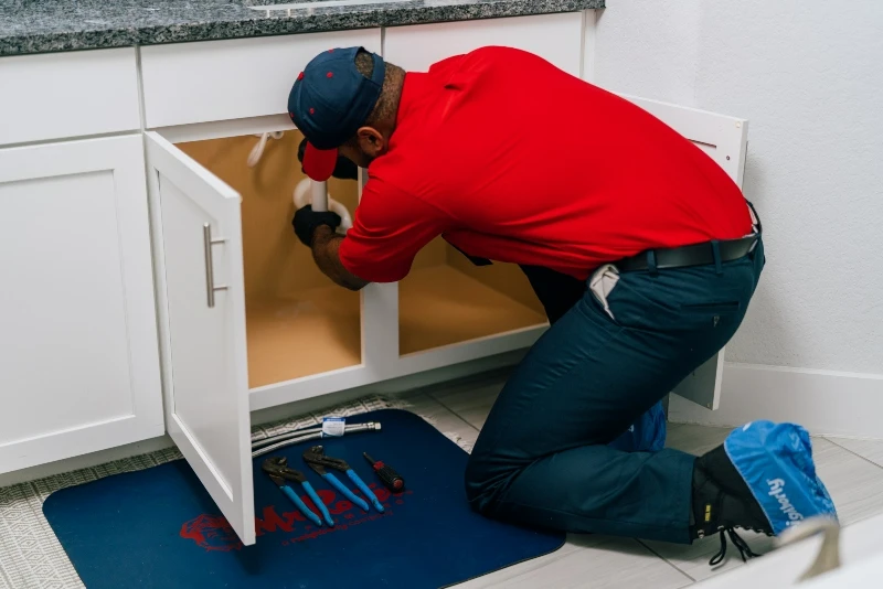 Mr. Rooter plumber fixing a pipe under a sink during a plumbing repair visit 