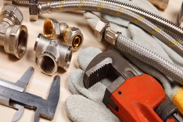 A collection of tools used by St. Albert plumbers, including a pipe wrench, pipe fittings, gloves, and several flexible water lines.