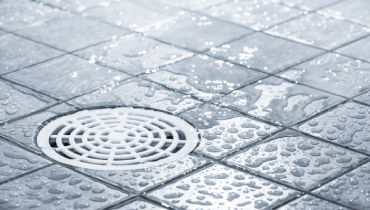 Shower drain with beads of water on gray tile.