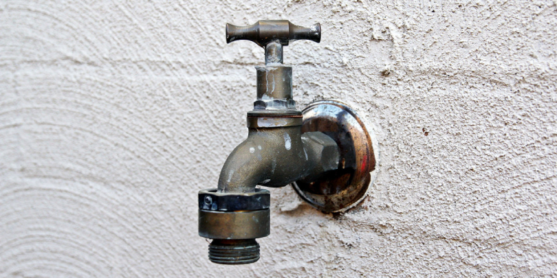 A close up image of an old hose bib on the exterior wall of a home.