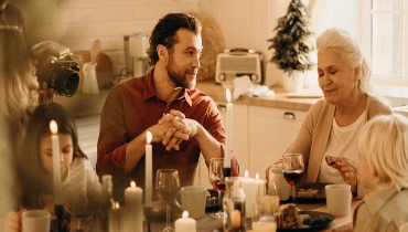 A family sits around the table during the holidays enjoying a meal; the grandmother is at the head of the table.