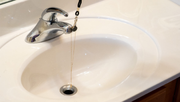 Necklace wrapped around a bathroom sink faucet and hanging into sink drain.