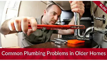 A plumber fixing under-sink pipes with a wrench.