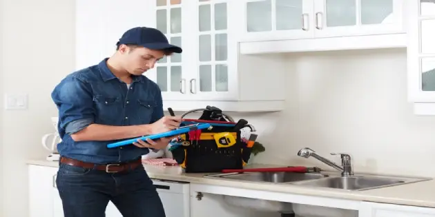 Professional plumber with clipboard standing by kitchen sink.