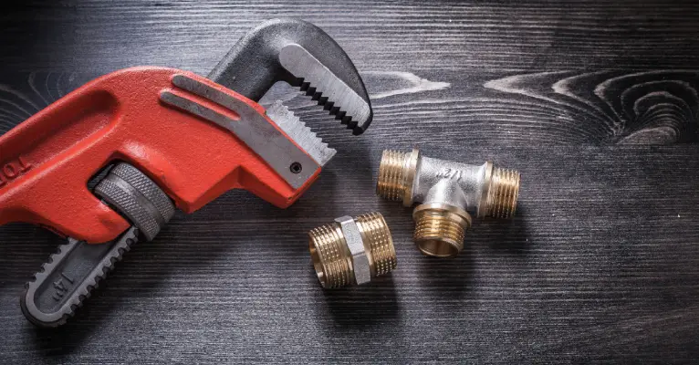 A monkey wrench and two pipe fittings lying on a dark wooden surface before being used by a plumber in Sherwood Park.