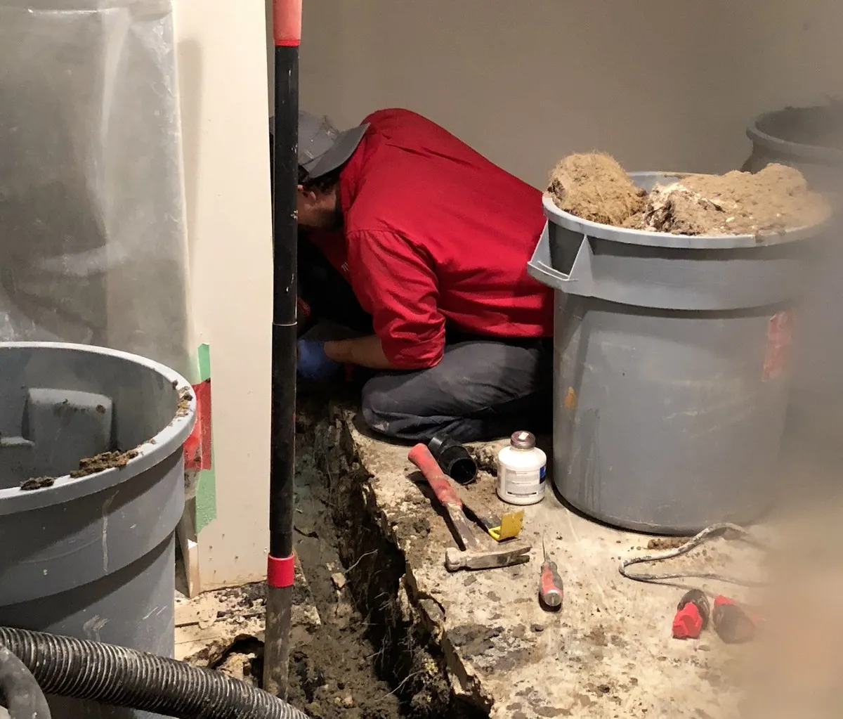 A plumber from Mr. Rooter Plumbing working on a pipe inside of a trench that’s been dug through the concrete foundation of a home inside the home’s basement.